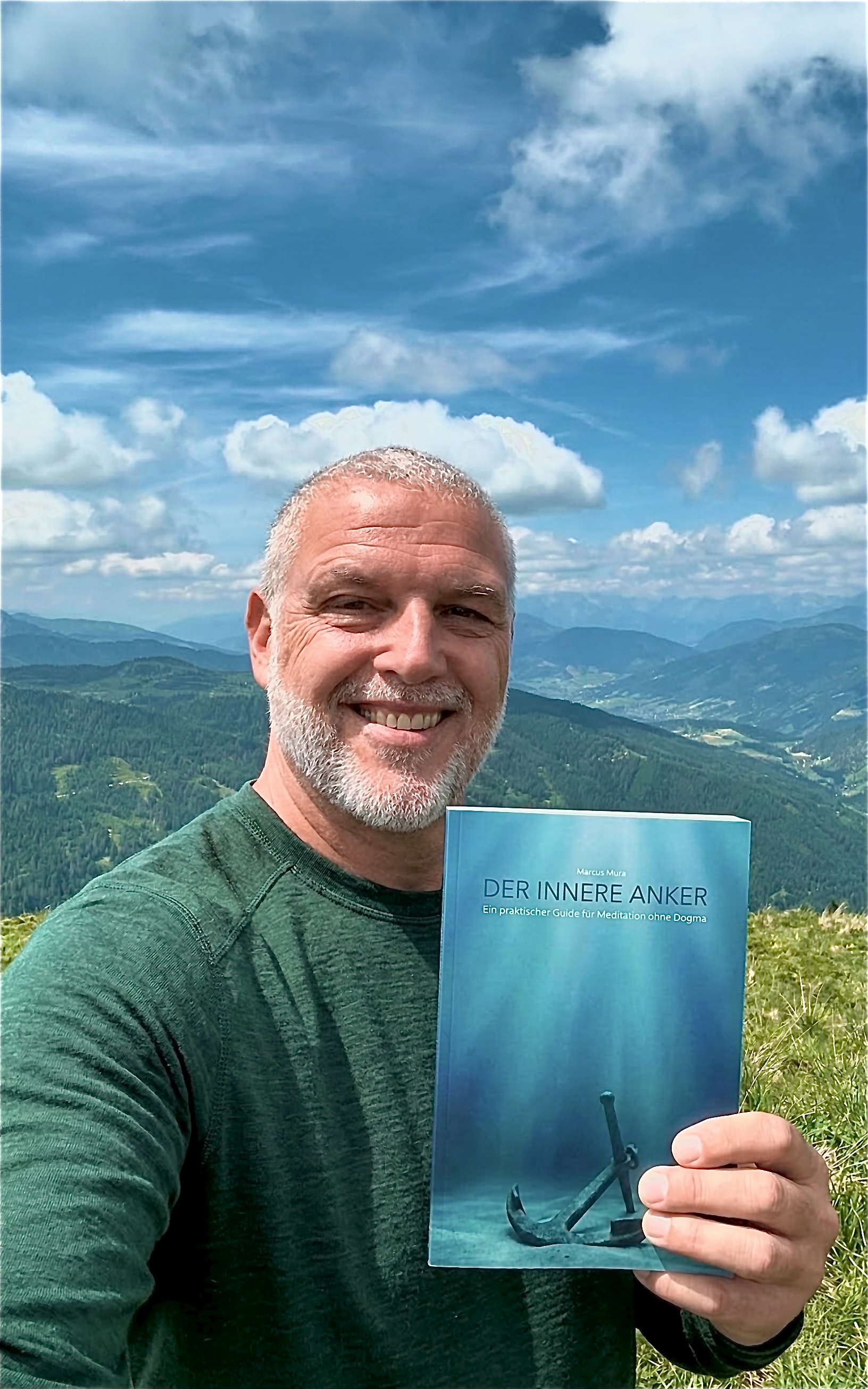 Marcus Mura, Autor von Der Innere Anker, hält sein Buch vor einem Bergpanorama